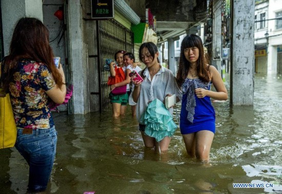 People walk on flooded road in typhoon-hit Haikou, capital of south China's Hainan Province, Sept. 16, 2014. Seawater flew backward into the city as typhoon Kalmaegi landed in the island province on Tuesday morning. (Xinhua/Jiang Jurong)