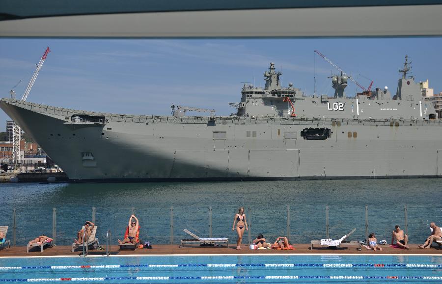 Sunbathers soak up rays beside a swimming pool in front of HMAS Canberra, which is berthed at Sydney's Garden Island naval base. The Canberra, the Royal Australian Navy's largest and most expensive warship, will be commissioned into service on Nov. 28. (Xinhua/AFP Photo) 