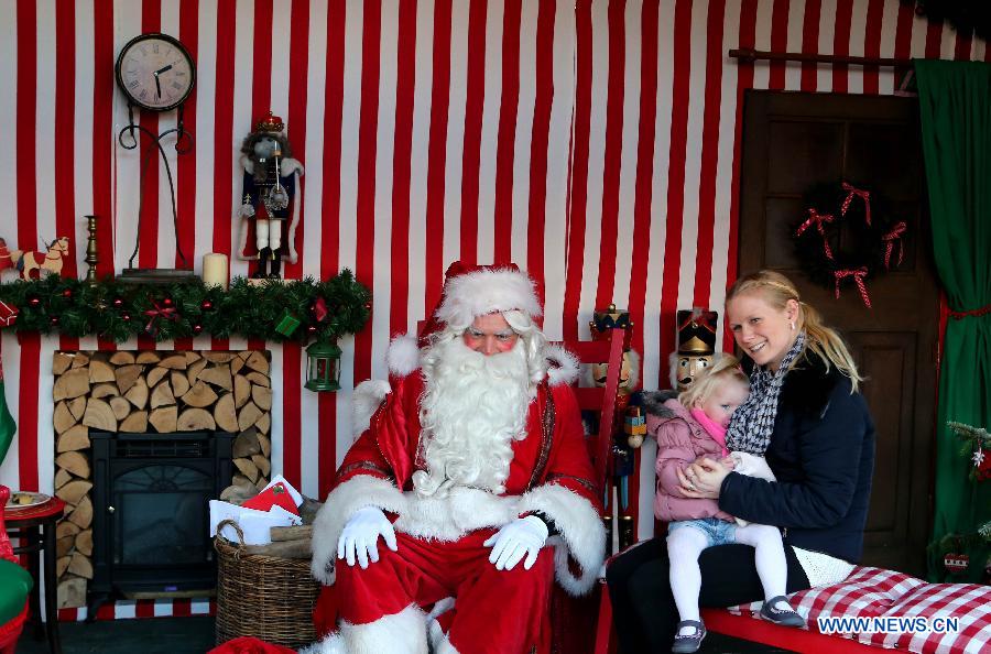 A mother carries her daughter to take a group photo with 'Santa Claus' at Hyde Park Winter Wonderland in London, Britain, on Nov. 24, 2014.