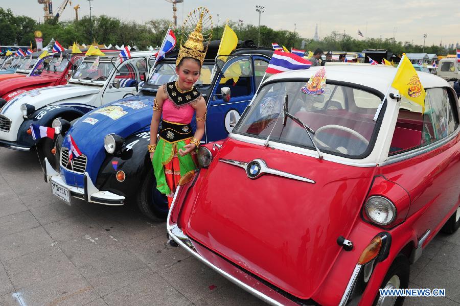 A girl poses for photos with antique cars during a parade as part of the celebration of Thai King's 87th Birthday Anniversary in front of Grand Palace in Bangkok, Thailand, Dec. 4, 2014. 