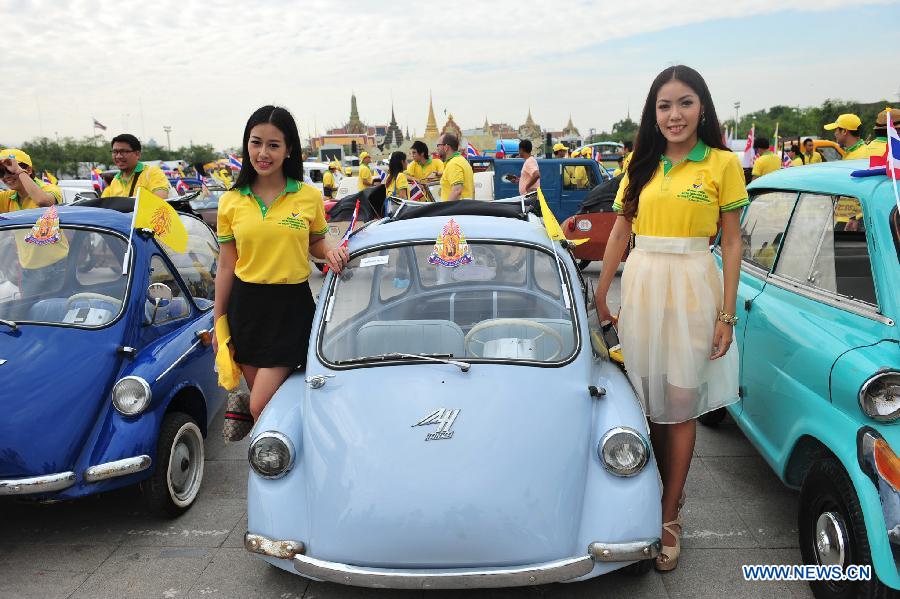 People pose for photos with antique cars during a parade as part of the celebration of Thai King's 87th Birthday Anniversary in front of Grand Palace in Bangkok, Thailand, Dec. 4, 2014.