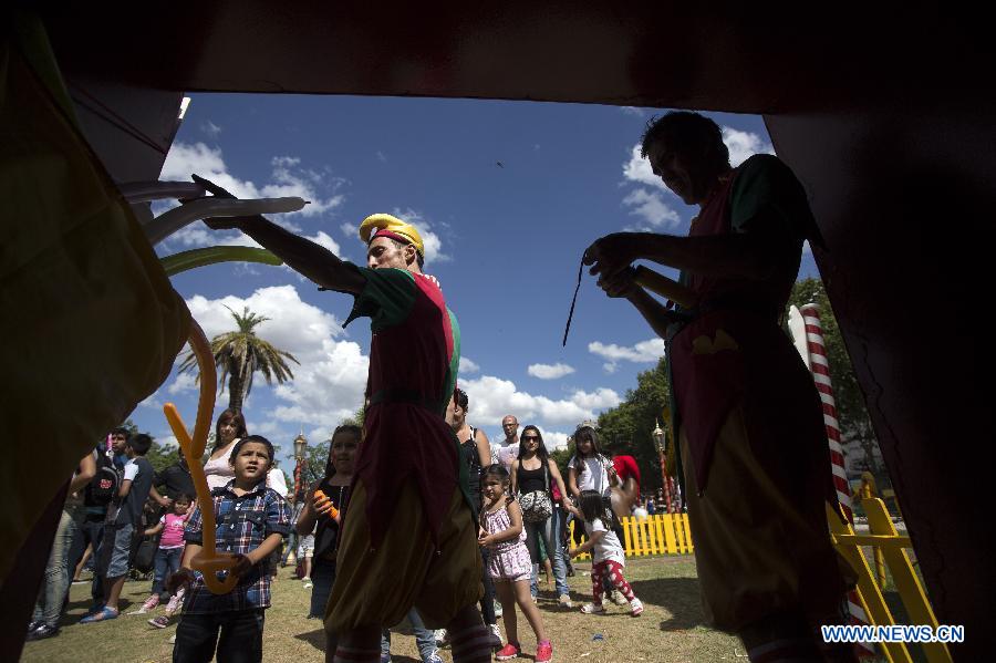 An actor dressed up as elves gives balloon figures to kids in the Christmas Park in Buenos Aires City, capital of Argentina, on Dec. 21, 2014. (Xinhua/Martin Zabala)