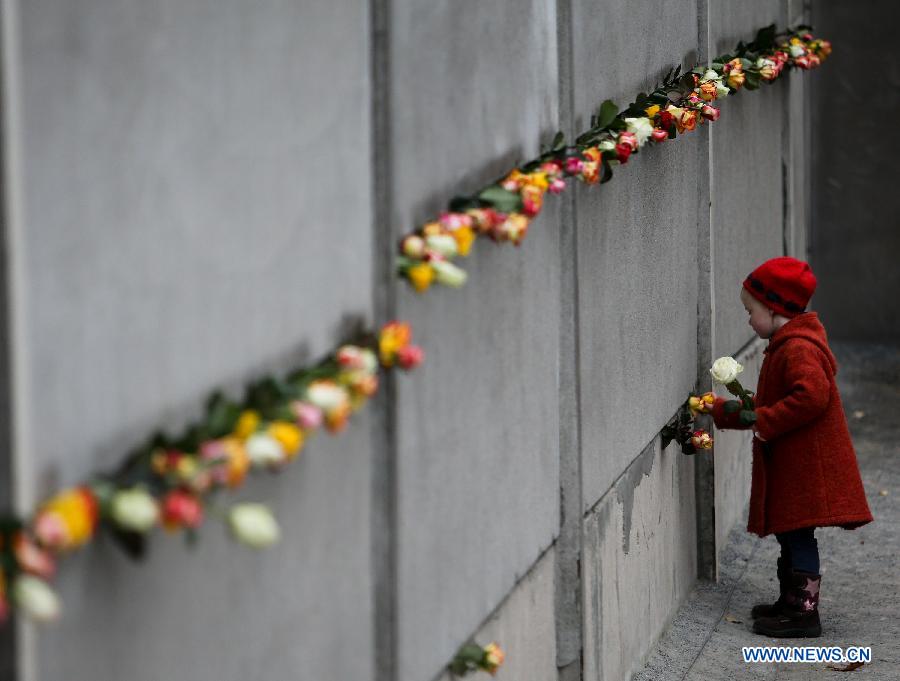 A girl puts flowers into a part of the former Belrin Wall during a memorial activity to commemorate the 25th anniversary of the fall of the Berlin Wall in Berlin, Germany, on Nov. 9, 2014.