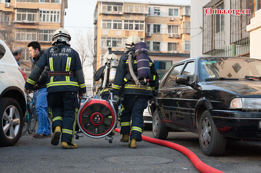 Firefighters prepare professional tools in trying to put out a fire in a residential area in downtown Beijing on Thursday, March 5, the traditional Chinese Lantern Festival. The blazing building is located between Linglong Rd. and Qixiancun Rd. in Haidian District, is used as a warehouse of Gehua, Beijing's local cable TV service provider. The burning rubber from the cable wire gives out a strong black smoke. [Photo by Chen Boyuan / China.org.cn]