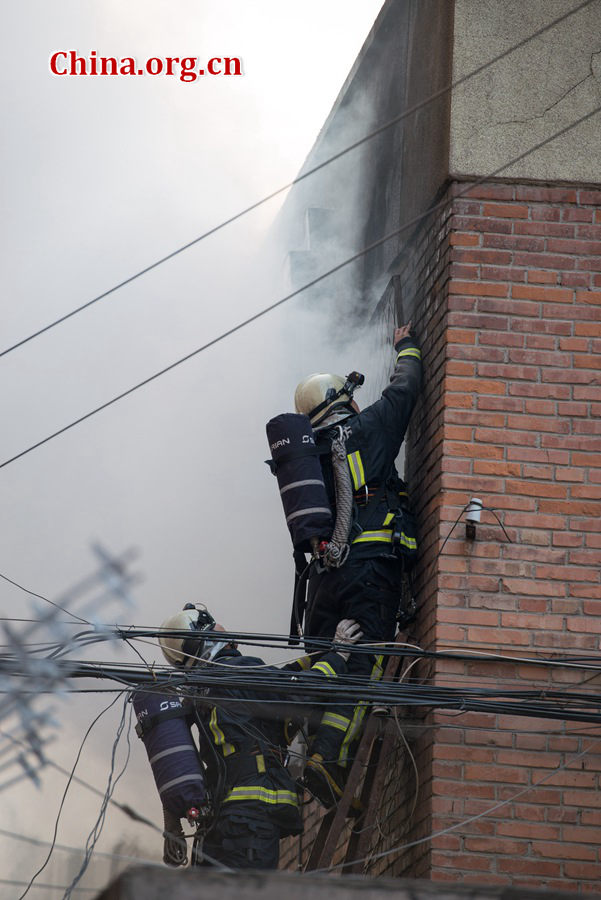 Firefighters try to break into a blazing building on Thursday, March 5, the traditional Chinese Lantern Festival. The building, according to people who live nearby, is used as a warehouse of Gehua, Beijing's local cable TV service provider, and the burning rubber from the cable gives out a strong black smoke. [Photo by Chen Boyuan / China.org.cn]