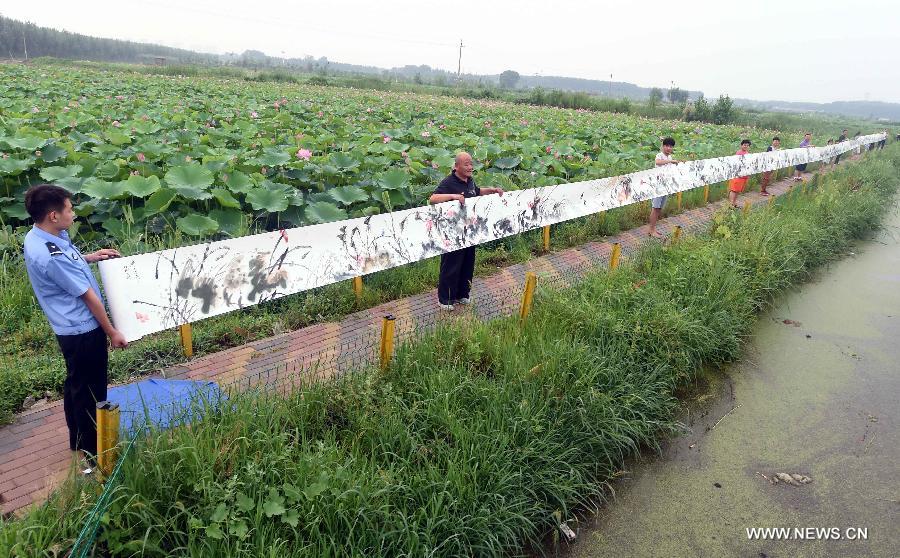 People hold a lotus painting for display before a lotus pond in Xianghe County of Langfang city, north China's Hebei Province, July 17, 2015. 