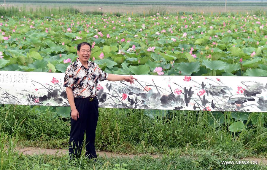 Wang Yongquan interprets his lotus painting to spectators before a lotus pond in Xianghe County of Langfang city, north China's Hebei Province, July 17, 2015. 