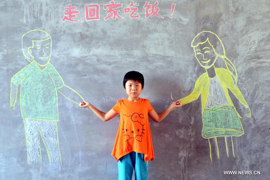 Liu Dongqing poses for photo with her parents painted on a blackboard in Nanguan Village of Chiping County, east China's Shandong Province, July 25, 2015. College students from the Academy of Fine Arts of Liaocheng University came to visit the 'left-behind' children and 'empty-nest' elderly persons, help them express their wish for family reunion with paintings. (Xinhua/Zhao Yuguo)  