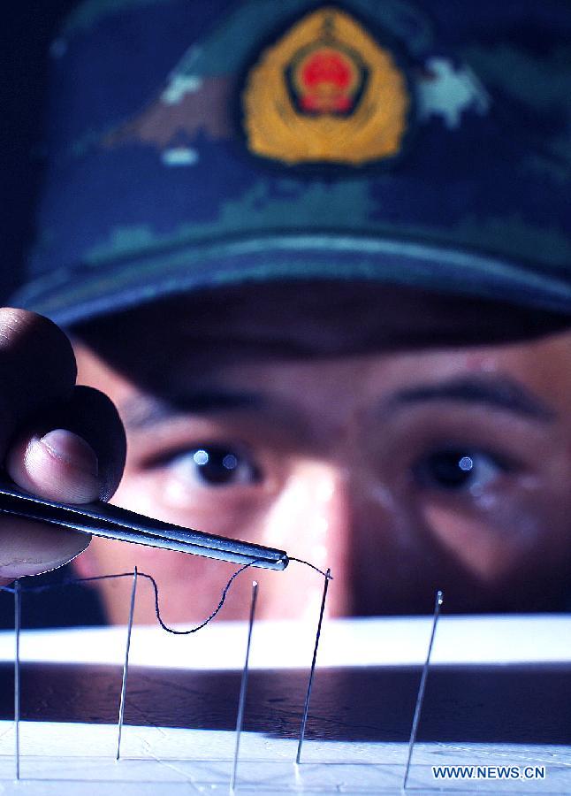 Xie Liuxiang, an Explosive Ordance Disposal(EDO) police, tries to thread a needle with tweezers during a training in east China's Shanghai Municipality, July 30, 2015. EDO police of Shanghai armed police unit continued their training as the heat wave scorched Shanghai. (Xinhua/Chen Fei) 