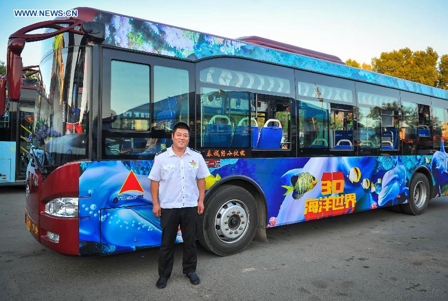 Bus driver Gu Zhenyu poses for a photo with his ocean theme bus in Changchun, northeast China's Jilin Province, Sept. 14, 2015. 