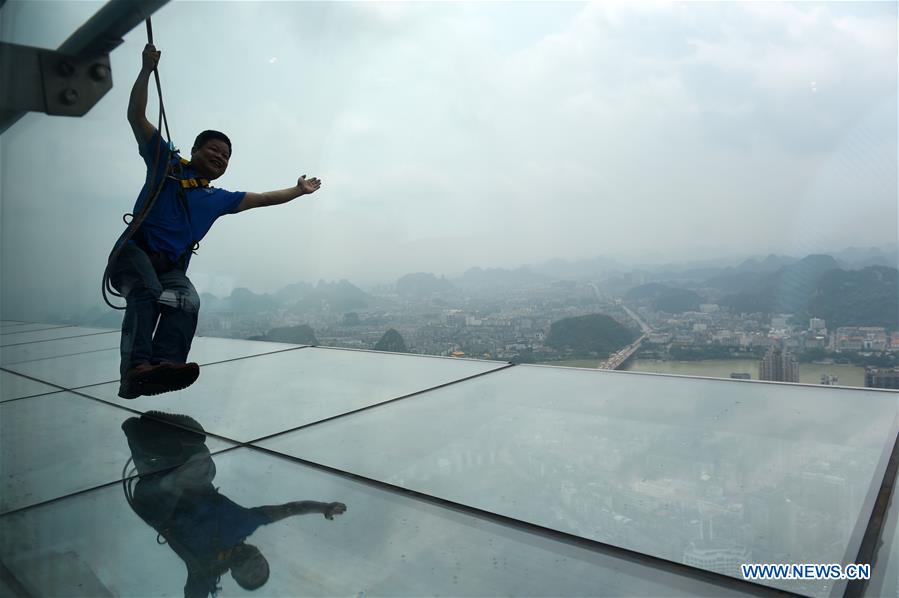 A tourist fastened by safty belt experiences sightseeing in the air on the Yunding glass-made plank road on a skyscraper in Liuzhou, south China's Guangxi Zhuang Autonomous Region, May 5, 2016. 