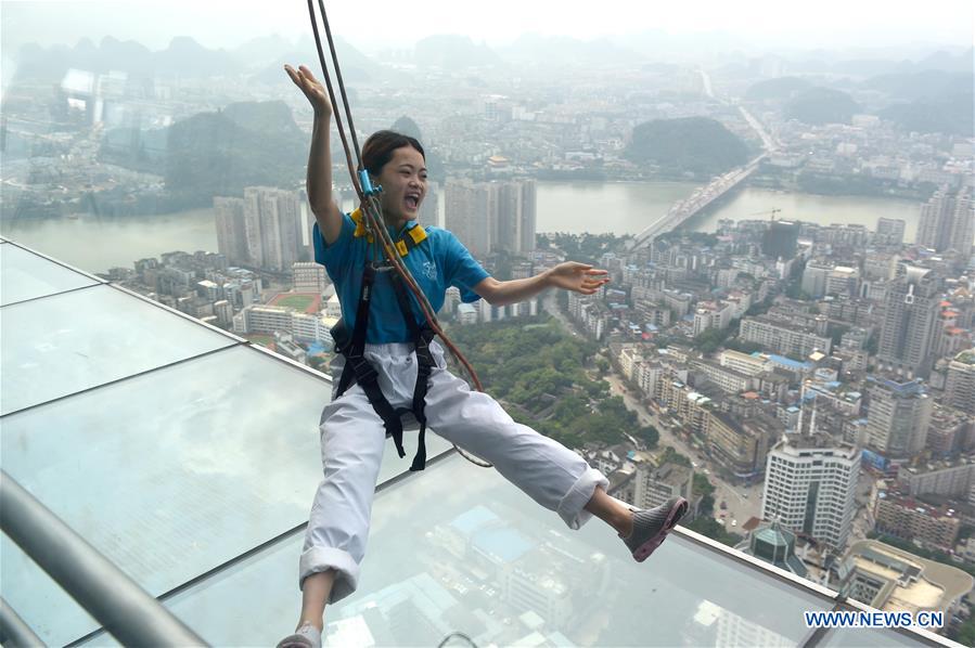 A tourist fastened by safty belt experiences sightseeing in the air on the Yunding glass-made plank road on a skyscraper in Liuzhou, south China's Guangxi Zhuang Autonomous Region, May 5, 2016. 