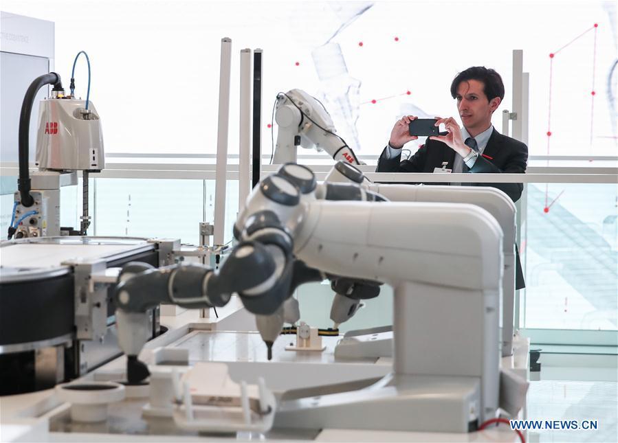 A staff member of the booth of ABB takes photos of displayed robotic arms during the 2019 Hanover Fair in Hanover, Germany, on April 1, 2019. With a total of 6,500 exhibitors from 75 countries and regions, the Hanover Fair shows the latest development of technologies for industrial use, including 5G network, artificial intelligence, light-weight manufacturing, among others. (Xinhua/Shan Yuqi)