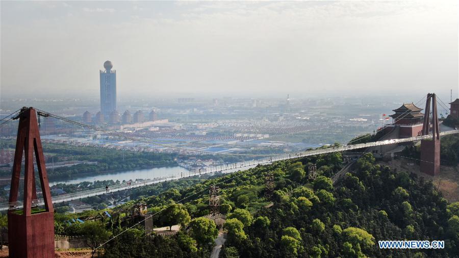 Aerial photo taken on May 4, 2019 shows tourists walking on a glass bridge at the Huaxi World Adventure Park in Huaxi Village of Jiangyin City, east China\'s Jiangsu Province. The 518-meter-long glass bridge hangs more than 100 meters above ground level at the park. It is made of panes of 35-mm-thick glass. Each glass can hold a maximum weight of 4.7 tonnes. Around 2,600 people can cross the bridge at a time. (Xinhua/Xu Congjun)